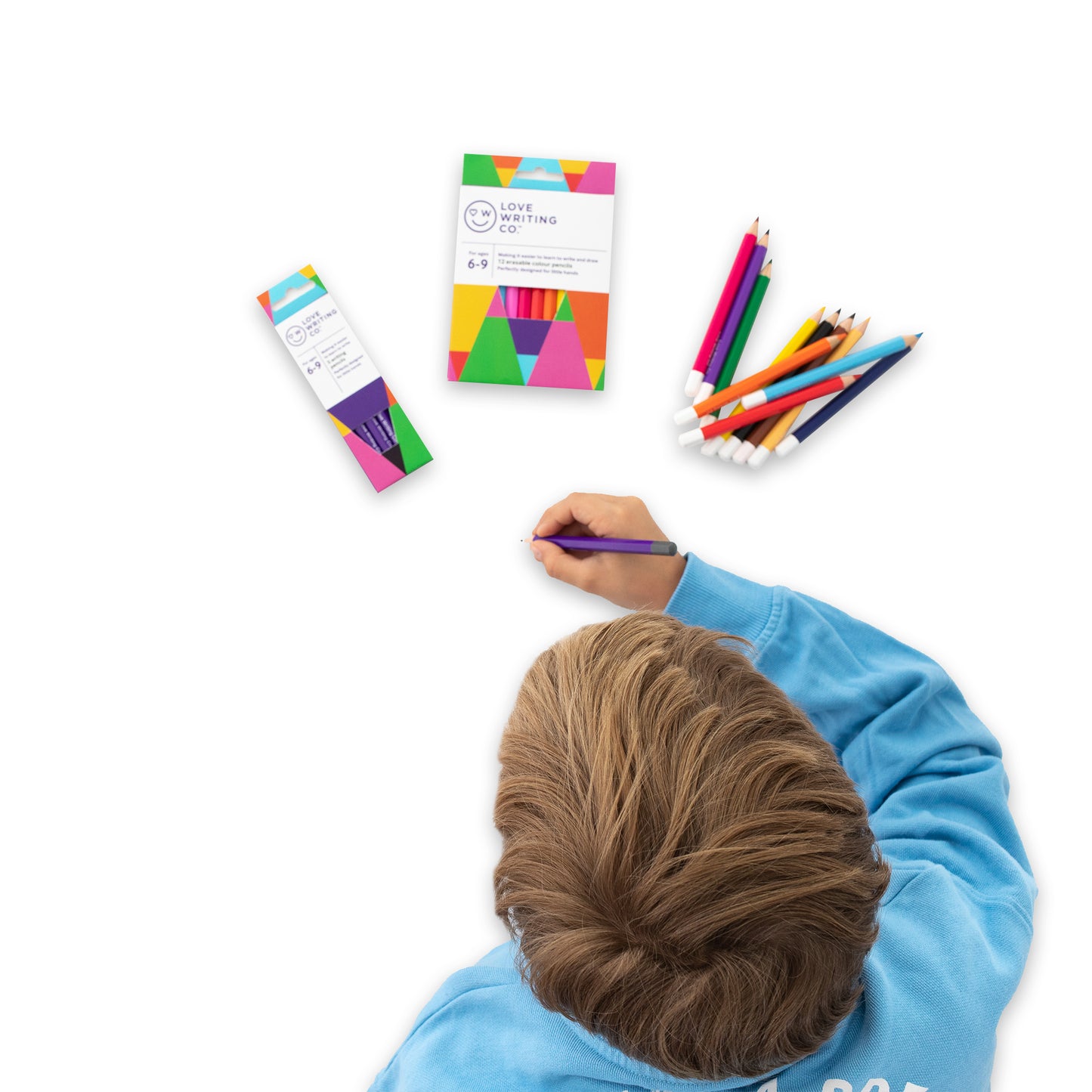 View from above of child writing with coloured pencils on workbook Colourful set of handwriting pencils for tripod grip 